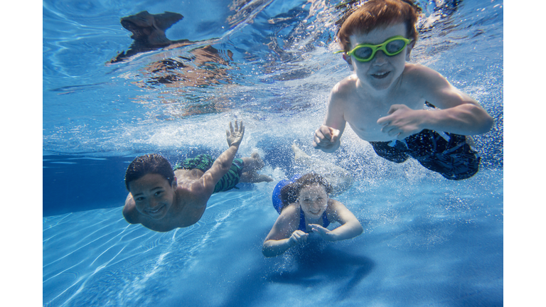 Three children swimming underwater, smiling at the camera.