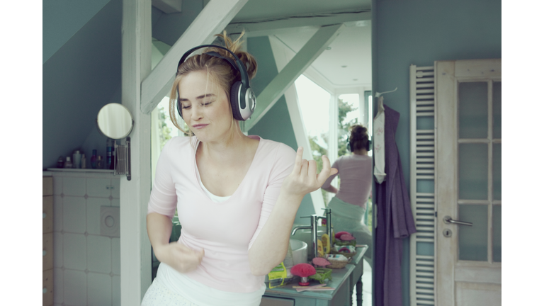 Young woman in bathroom with headphones playing air guitar