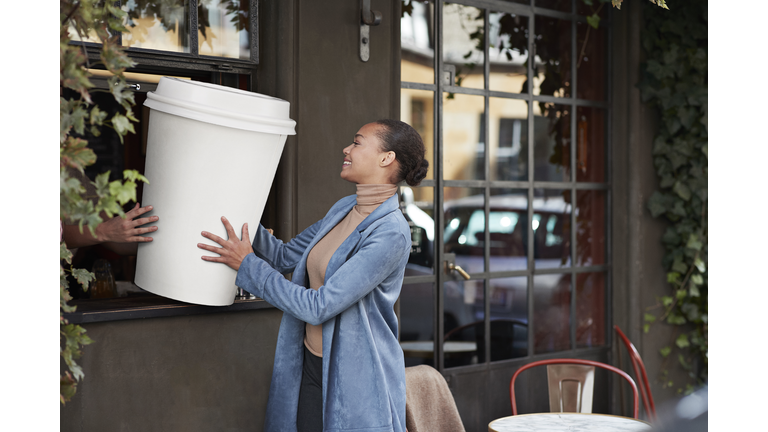 Woman holding large disposable coffee cup at take away counter of cafe