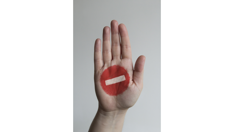 Close-up of stop sign painted on mans hand against gray background