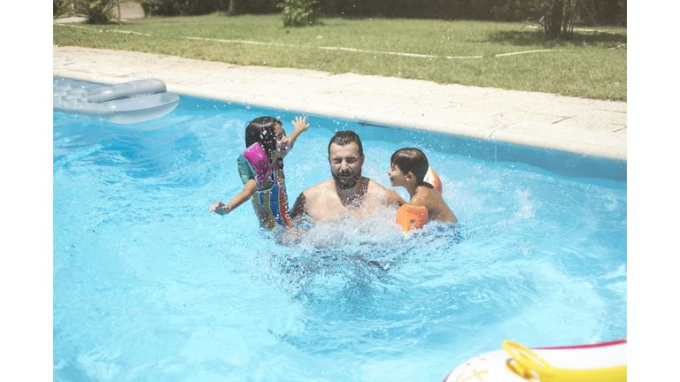 bearded 38 years Father playing with his children in swimming pool in summer day.