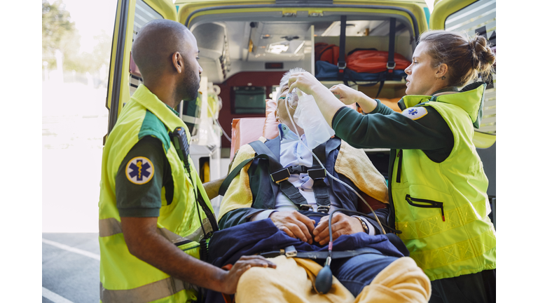 Male and female paramedics treating businessman with CPR outside ambulance