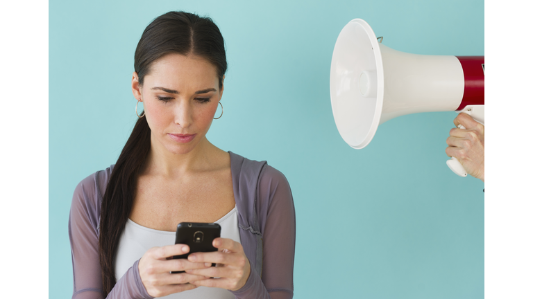 Studio shot of woman texting and ignoring voice from bullhorn