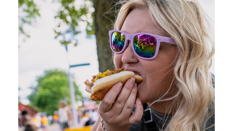 Blonde woman eats and chows down a footlong hot dog at the state fair in Minnesota