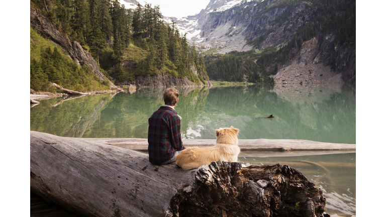 Rear view of man and dog sitting on fallen tree at Blanca Lake