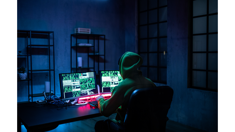 Hacker man working on computers in dark room, rear view.