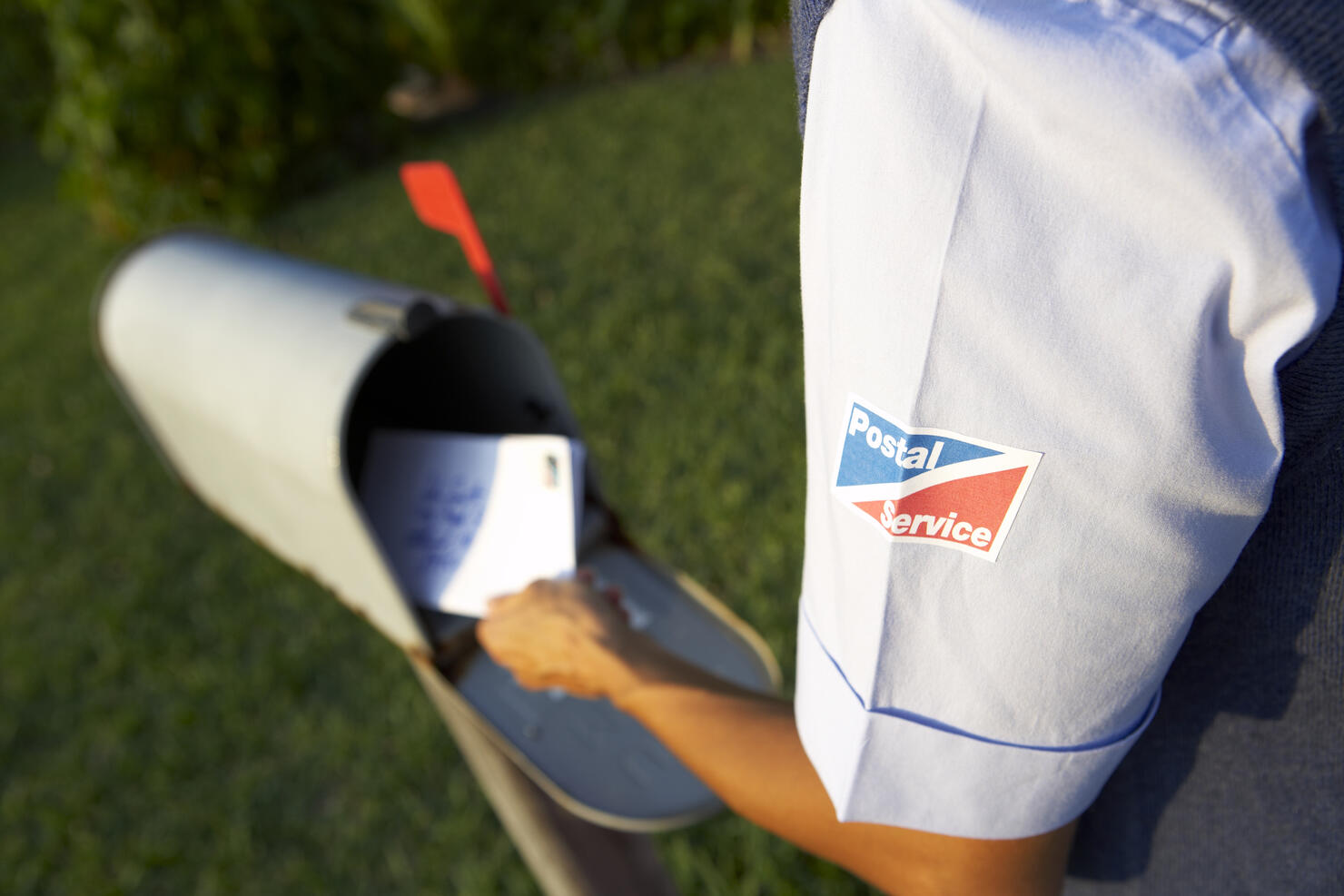 Postal worker putting mail into mailbox, mid section, rear view