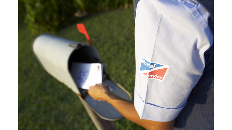 Postal worker putting mail into mailbox, mid section, rear view