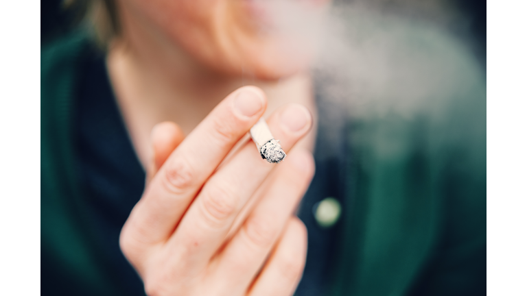 Unrecognizable woman wrapped in cigarette smoke holding a lit cigarette in her hand