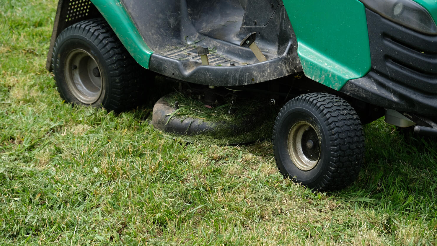 Green grass trimming with lawn mower. Tractor mowing grass in a public park. Close-up view of the lawn mower dirty blade after mowing the lawn. Professional lawn mower cuts the grass.
