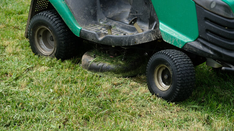 Green grass trimming with lawn mower. Tractor mowing grass in a public park. Close-up view of the lawn mower dirty blade after mowing the lawn. Professional lawn mower cuts the grass.