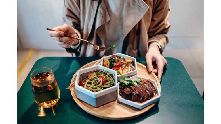 Close up of young Asian woman enjoying fusion food in a stylish restaurant. The meal set is freshly served on a  wooden tray with various nutritional ingredients to create a balanced and healthy diet. Farm-to-table, healthy eating concept