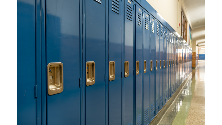 Photo of a blue metal lockers along a nondescript hallway in a typical US High School. No identifiable information included and nobody in the hall.