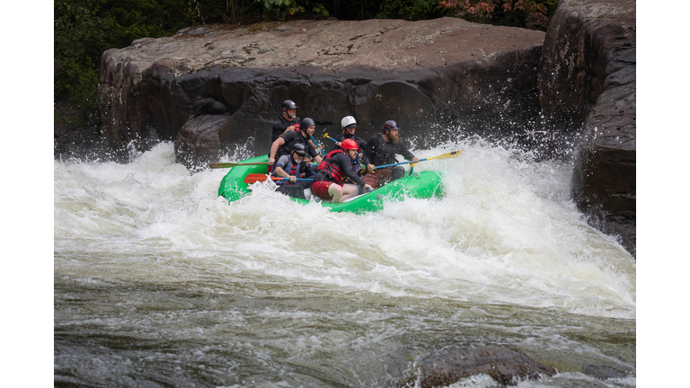 People in an inflatable boat riding a rushing river's wave. Rafting in Fayetteville, West Virginia.