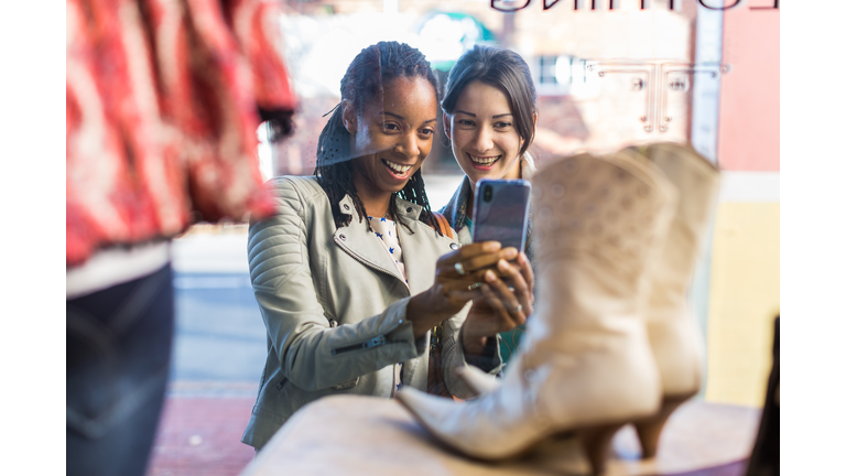 Two female friends photographing display in vintage clothes shop window