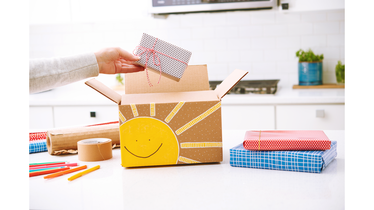 Woman adding a gift to a handmade gift box with cute sunshine design. Concept of shipping happiness.