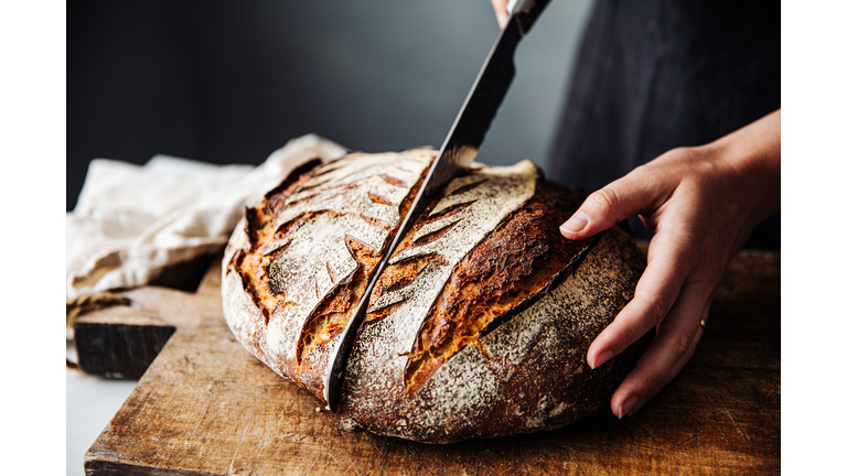 Woman cutting sourdough bread with knife on board