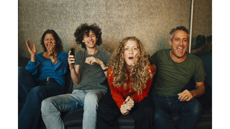 Happy parents and children cheering while watching sports in living room at night