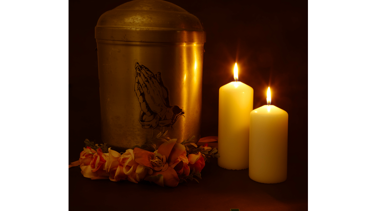 Funeral urn with praying hands and burning candles.