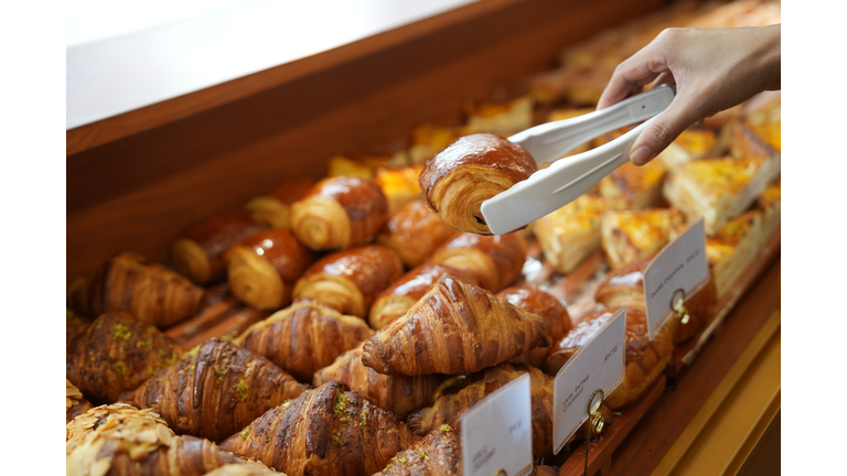 Close-up woman choosing pastry from a bakery store selecting holding a tray and service tong