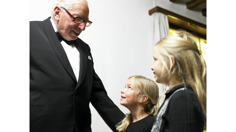 Senior man in tuxedo talking with girls (5-7), smiling, side view