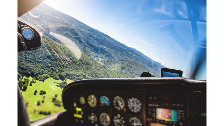 Small airplane cockpit interior in selective focus with control instrument panel and hilly landscape background in summer