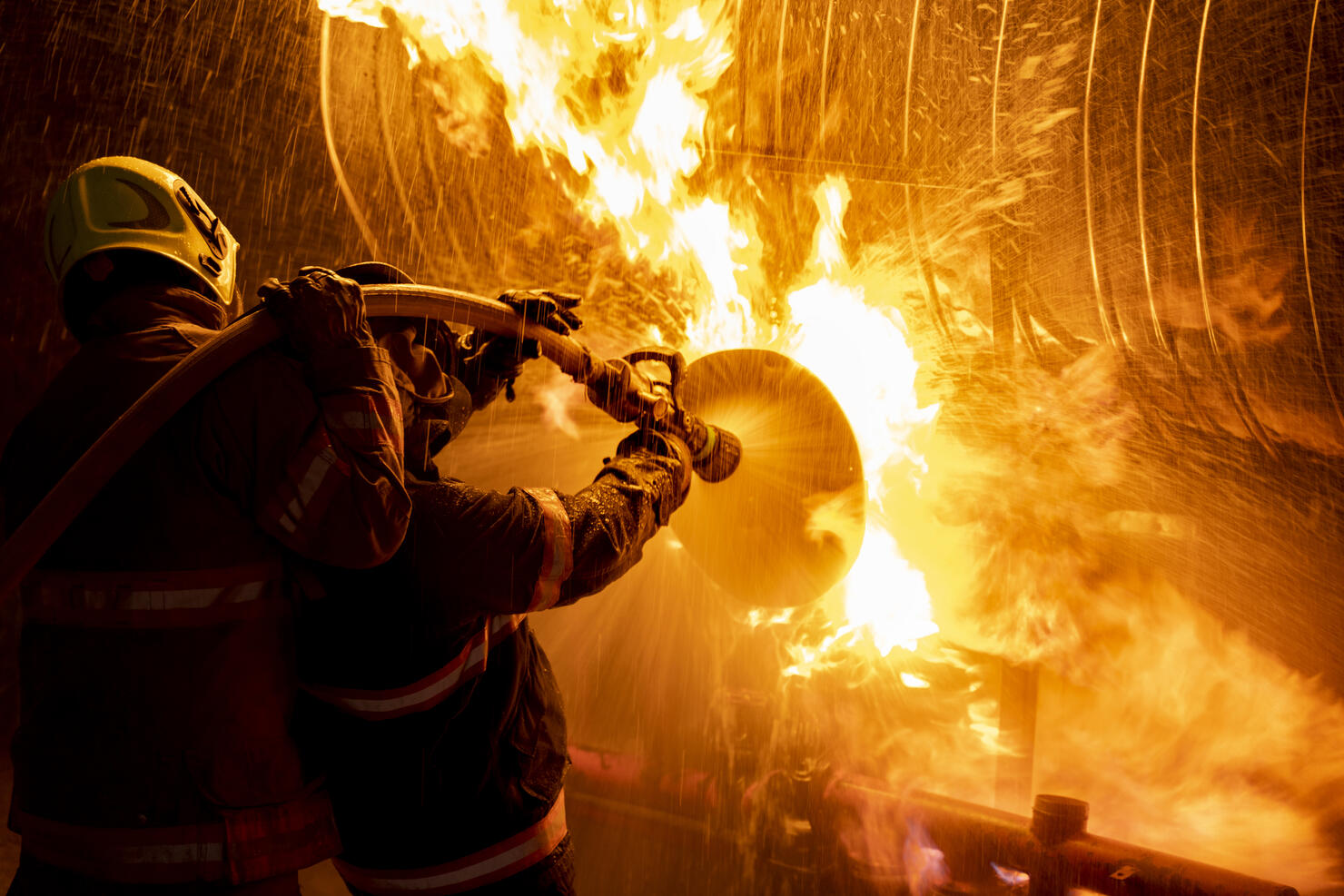 Firefighter in fire fighting suit spraying water, Firemen fighting raging fire with huge flames of burning, Fire prevention and extinguishing concept
