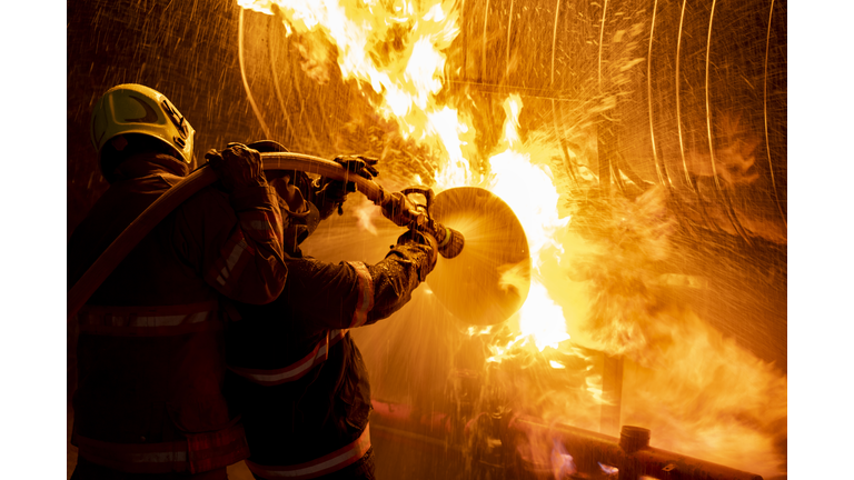 Firefighter in fire fighting suit spraying water, Firemen fighting raging fire with huge flames of burning, Fire prevention and extinguishing concept