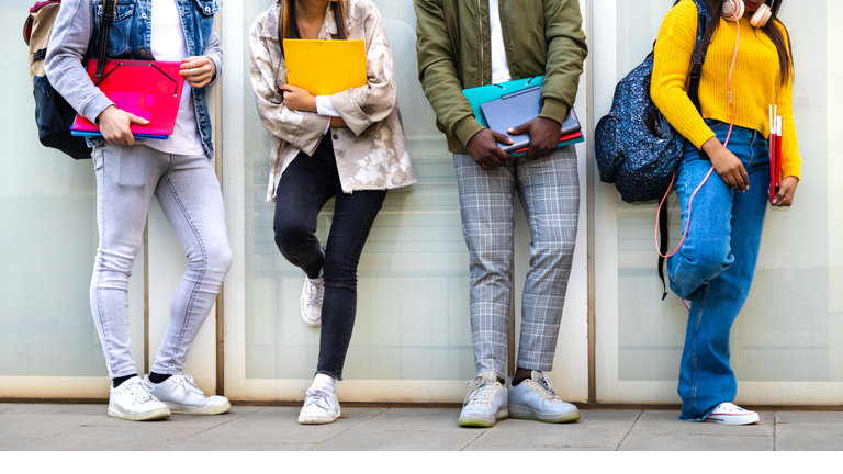 Group of multiracial teenage college students ready to go back to school standing against blue background wall.