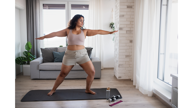 Portrait of beautiful young overweight woman indoors at home,  doing exercise.