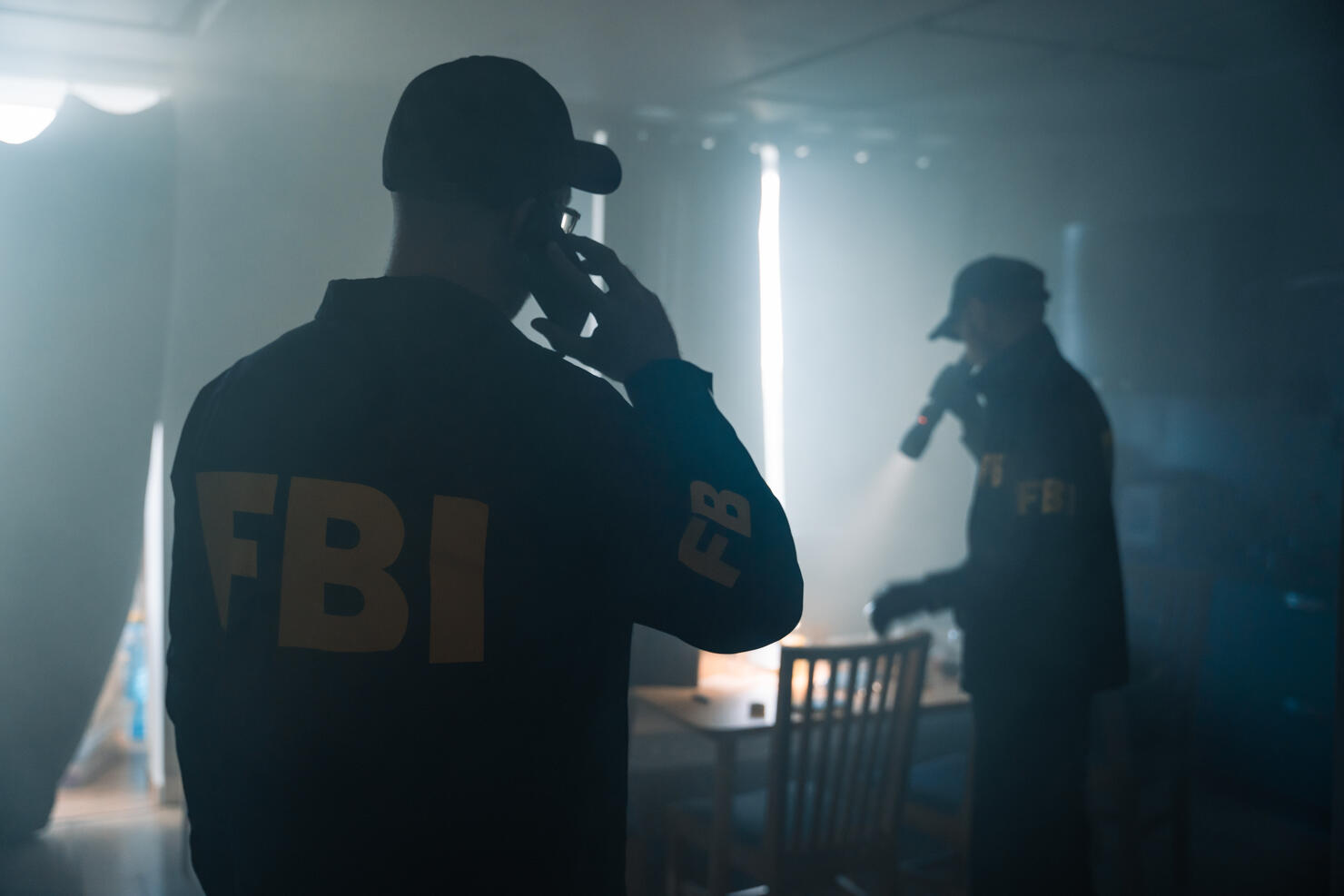 Action movie scene with two FBI agents at the crime scene in a fogged room of criminal's apartment, calling criminologists
