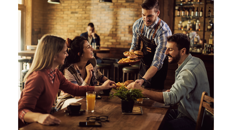 Happy waiter serving food to group of friends in a pub.