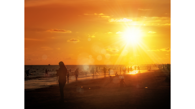 silhouetted people on public beach over orange colored sunset sky