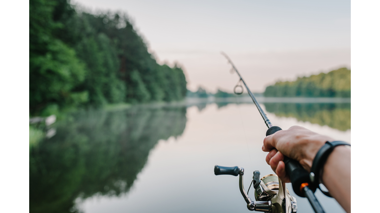 Fisherman with rod, spinning reel on the river bank. Sunrise. Fishing for pike, perch, carp. Fog against the backdrop of lake. background Misty morning. wild nature. The concept of a rural getaway.