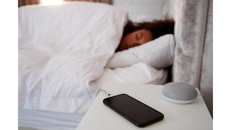 Woman Asleep In Bed With Mobile Phone And Voice Assistant On Bedside Table