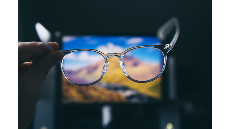 Selective focus on transparent clear blue light computer glasses and computer screen glowing on the background in home or office. Blue light glasses protect eyes and eyesight from screens blue light.