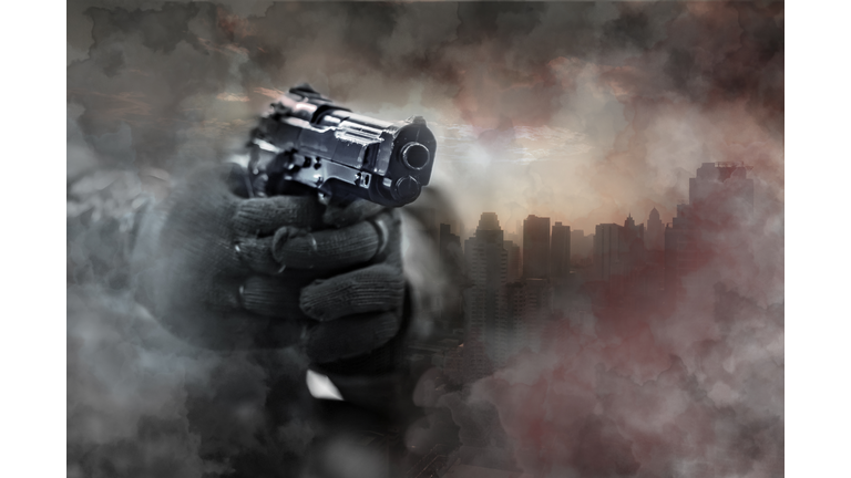 Gun in gunman's hand with city background.