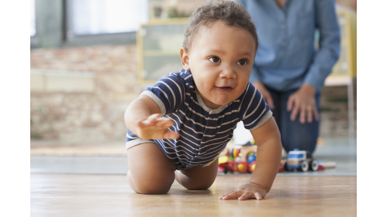 Hispanic grandmother watching baby grandson crawling on floor