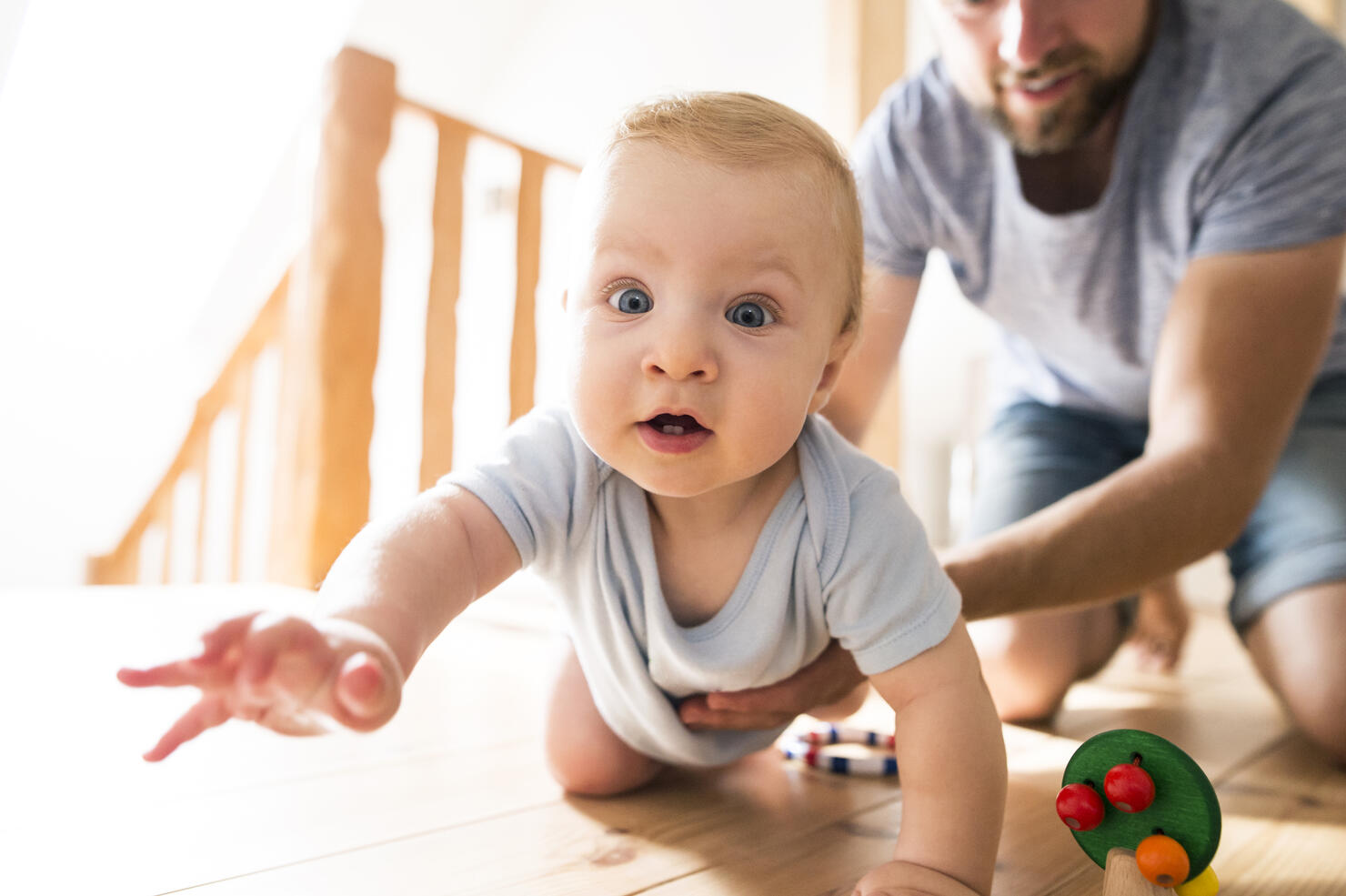 Father supporting crawling baby at home