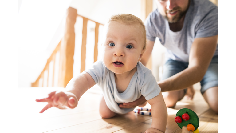 Father supporting crawling baby at home