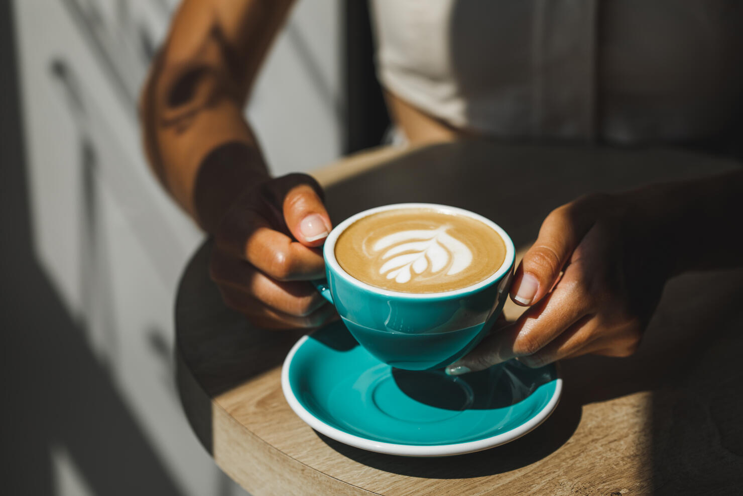 Woman hands holding cup of fresh cappuccino close up. Beautiful natural sun light in cafe