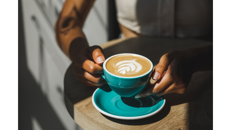 Woman hands holding cup of fresh cappuccino close up. Beautiful natural sun light in cafe