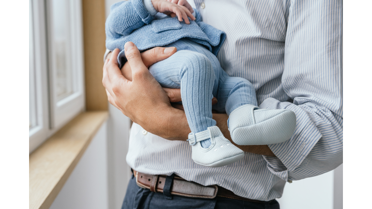 Cropped close-up of father holding baby by window at home