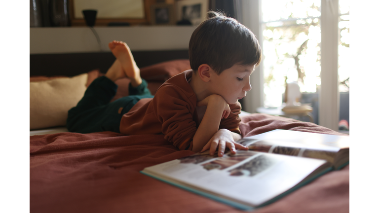 A 7 year old boy reading, laying on his parents bed