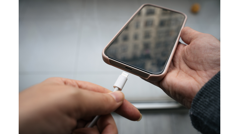 Close-up of a hand connecting the charging cable to the cell phone