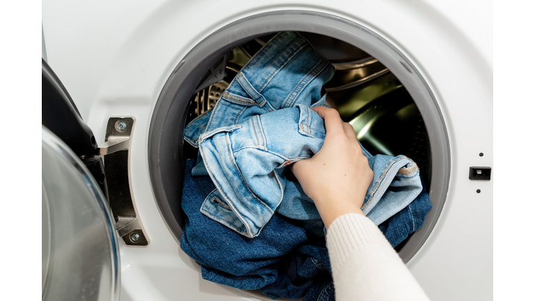 Person putting jeans into the drum of a washing machine, front view. Washing dirty jeans in the washer