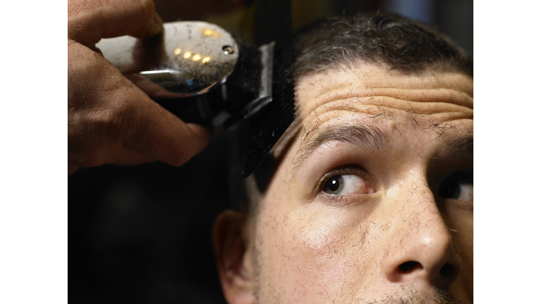 Barber shaving man's hair with electric razor, close-up