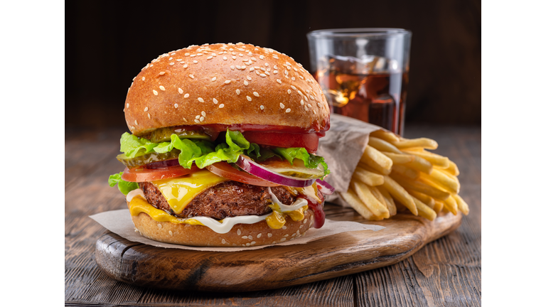 Tasty cheeseburger, glass of cola and french fries on wooden tray close-up.