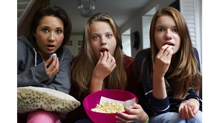 Teenage girls watching horror movie with popcorn