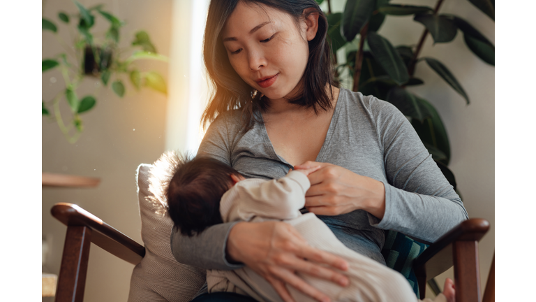 Mother breastfeeding baby on arm chair in living room